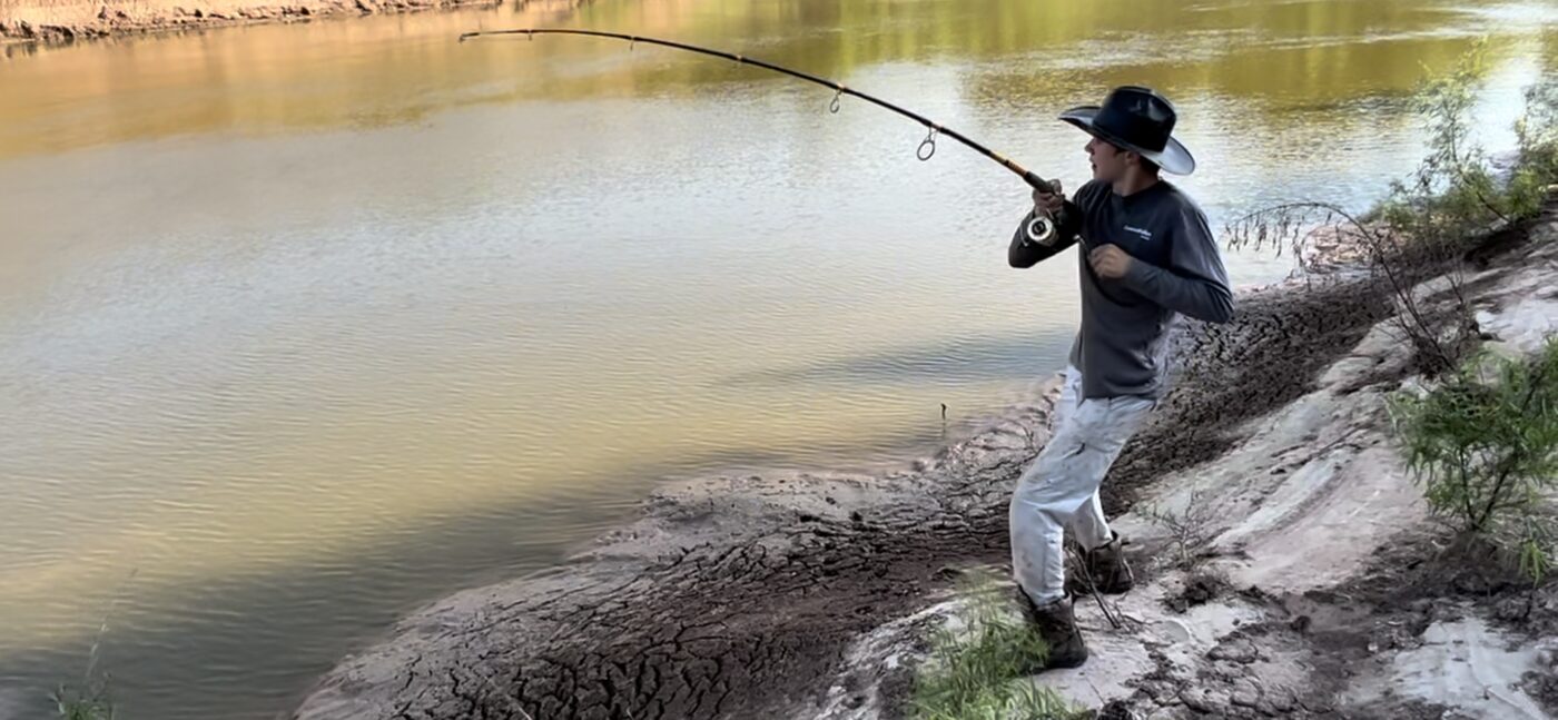 Angler fighting a fish from a riverbank