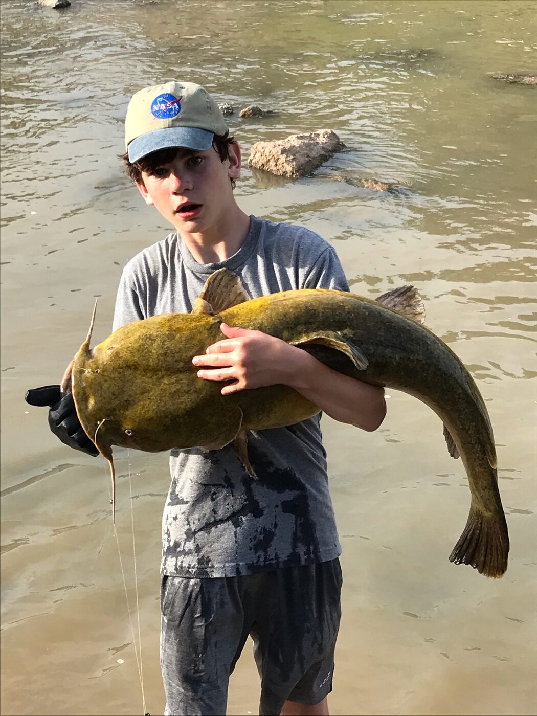Logan holding a large catfish beside the water