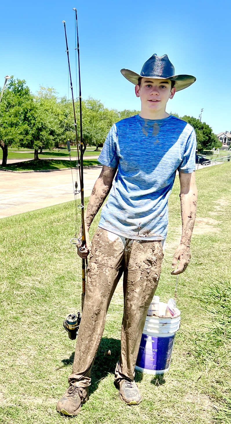 Logan wearing his cowboy hat and holding fishing rods after a muddy day of fishing